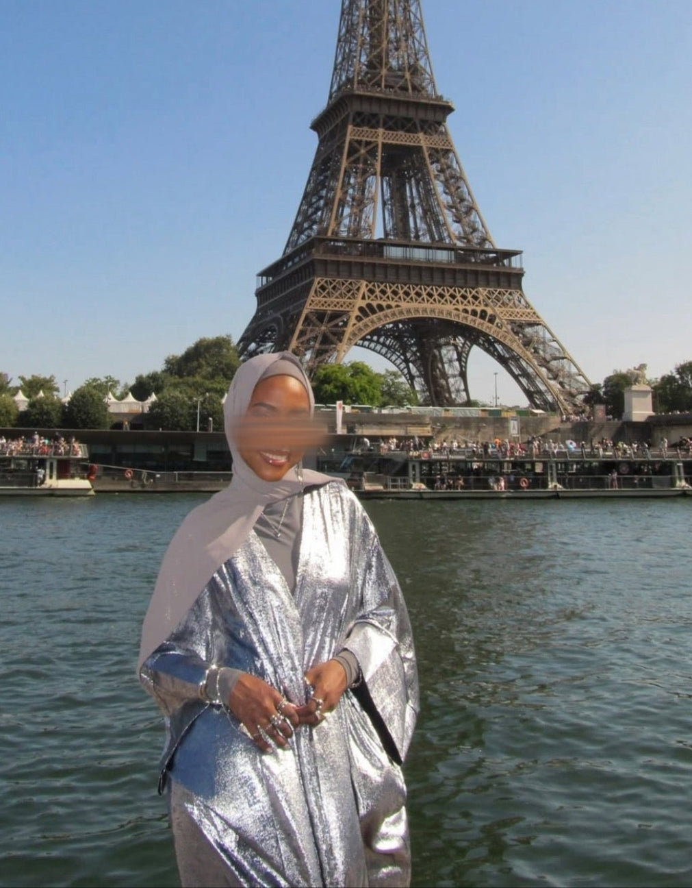 Person wearing a silver crushed velvet abaya standing in front of the Eiffel Tower with blurred face