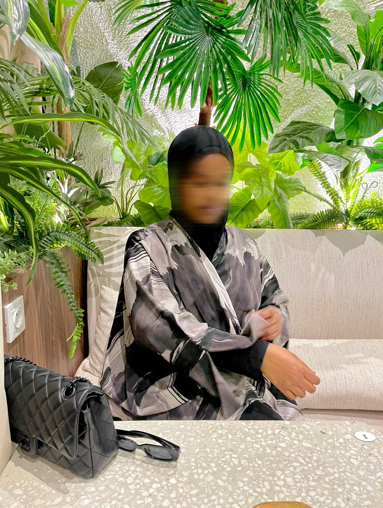 Person sitting on a couch with plants in the background wearing a grey marble abaya with black hijab
