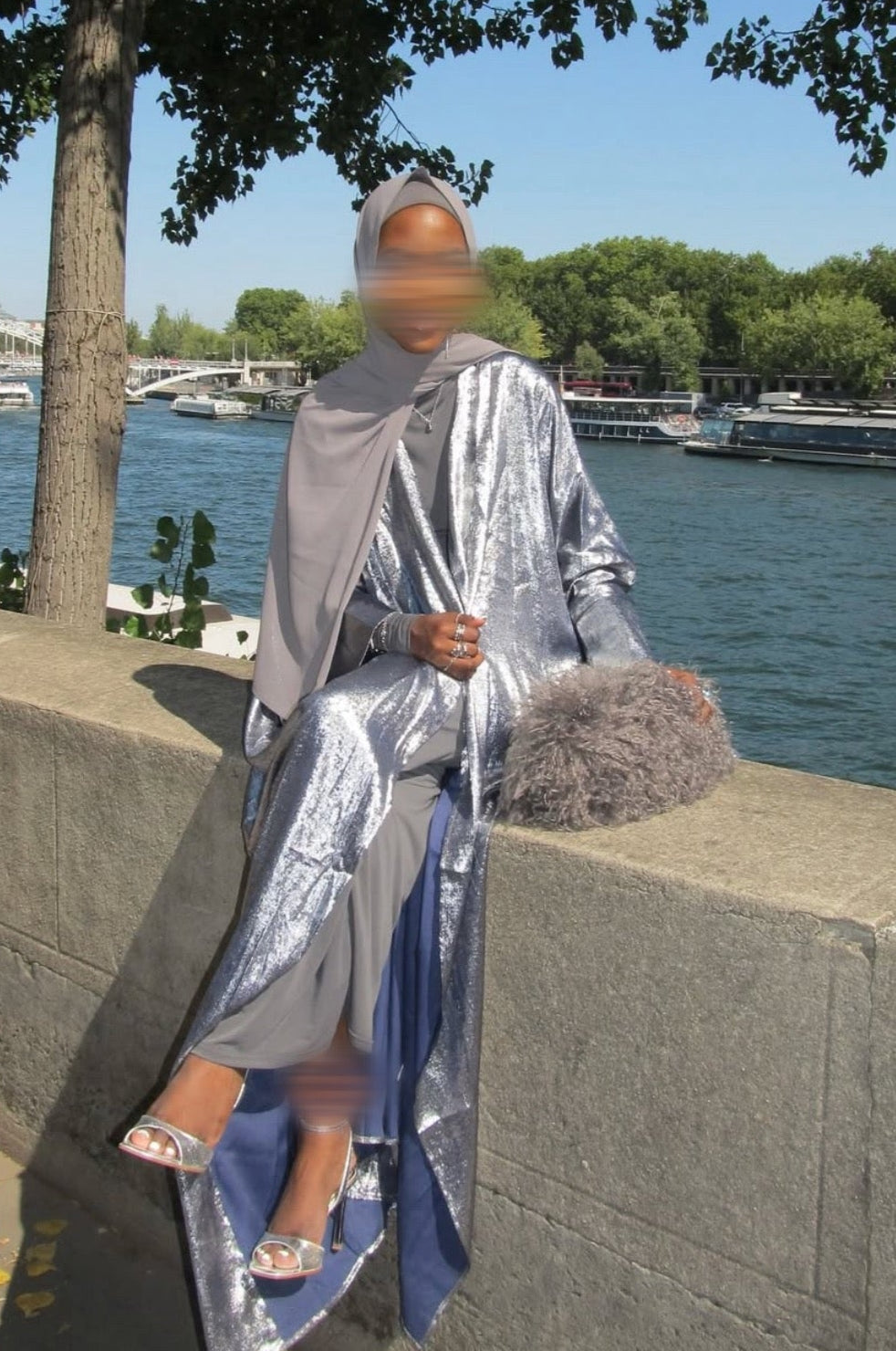 Person wearing a silver crushed velvet abaya by a waterfront with trees and water in the background.