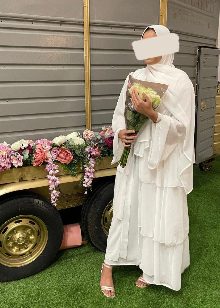 a model wearing a white abaya with a white hijab holding a bouquet of flowers