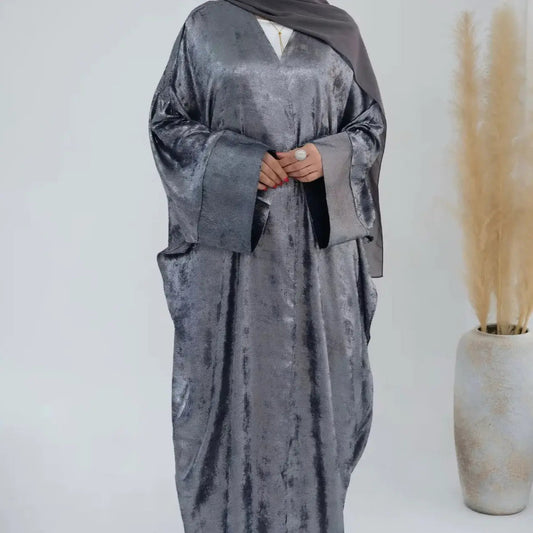 Grey crushed velvet abaya dress worn by a person on a white background with a vase of dried plants.